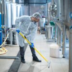 Professional industrial cleaner in protective uniform cleaning floor of food processing plant.